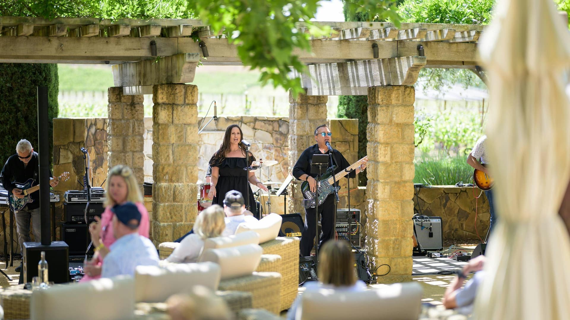Outdoor band performance under pergola with seated audience.