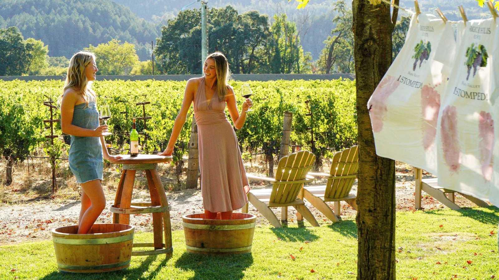 Two women wine tasting beside vineyard grape-stomping barrels