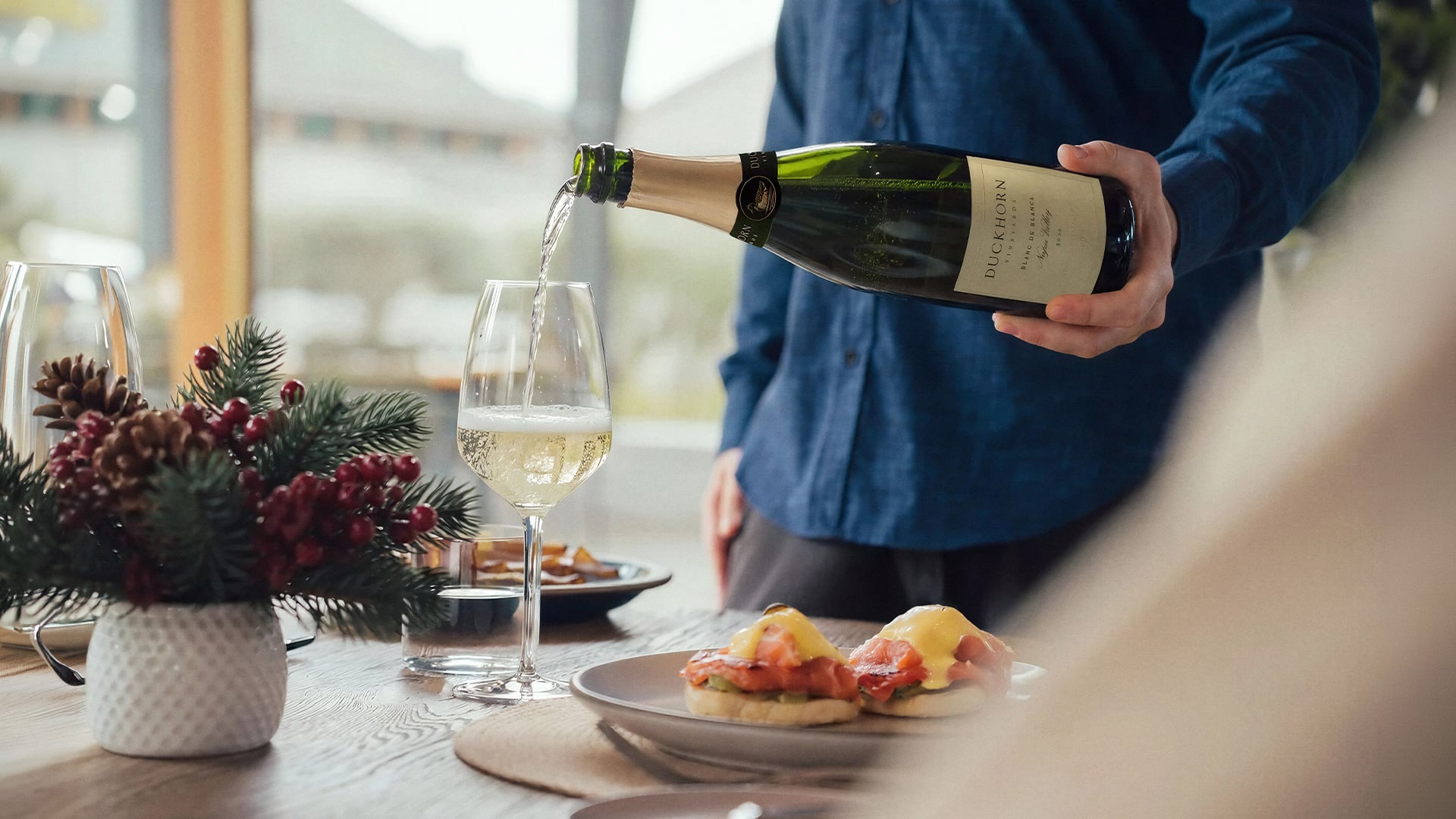 Person pours sparkling wine into glass beside brunch dishes