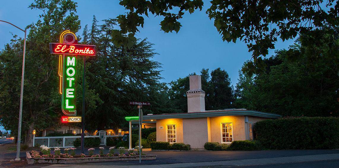 Retro neon motel sign at dusk with trees.