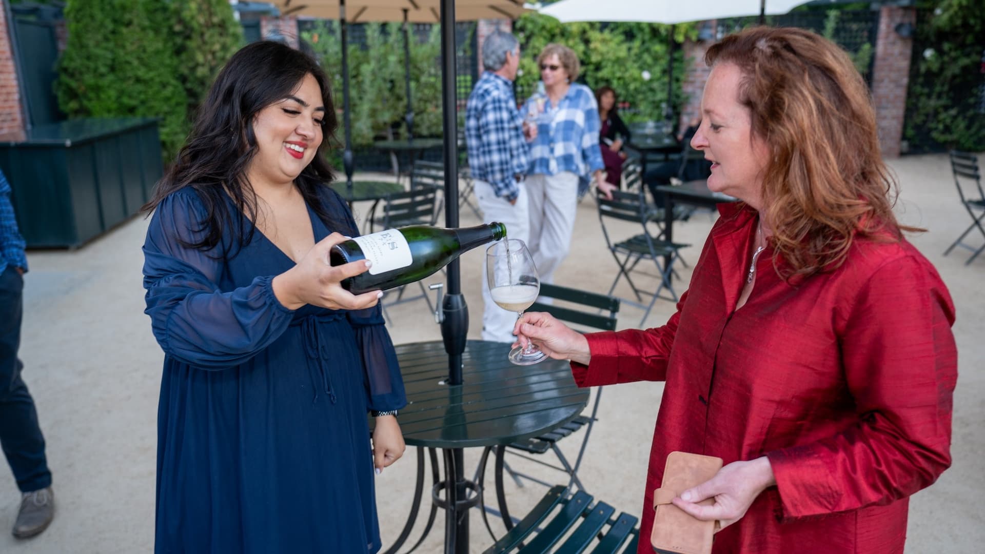 Women pouring wine outdoors at a gathering.