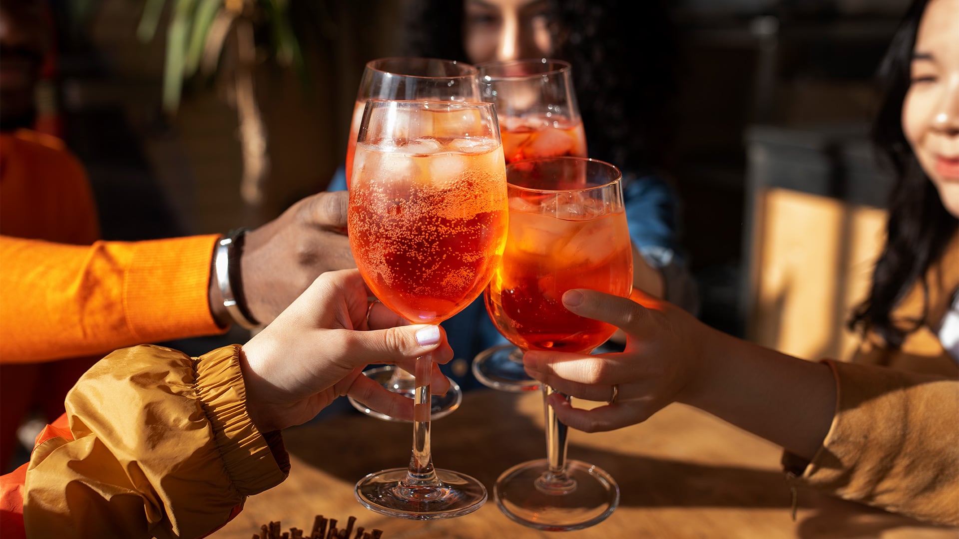 Friends clink glasses of orange cocktails in sunlight