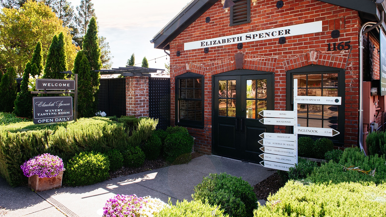 Brick winery tasting room with garden and signs.