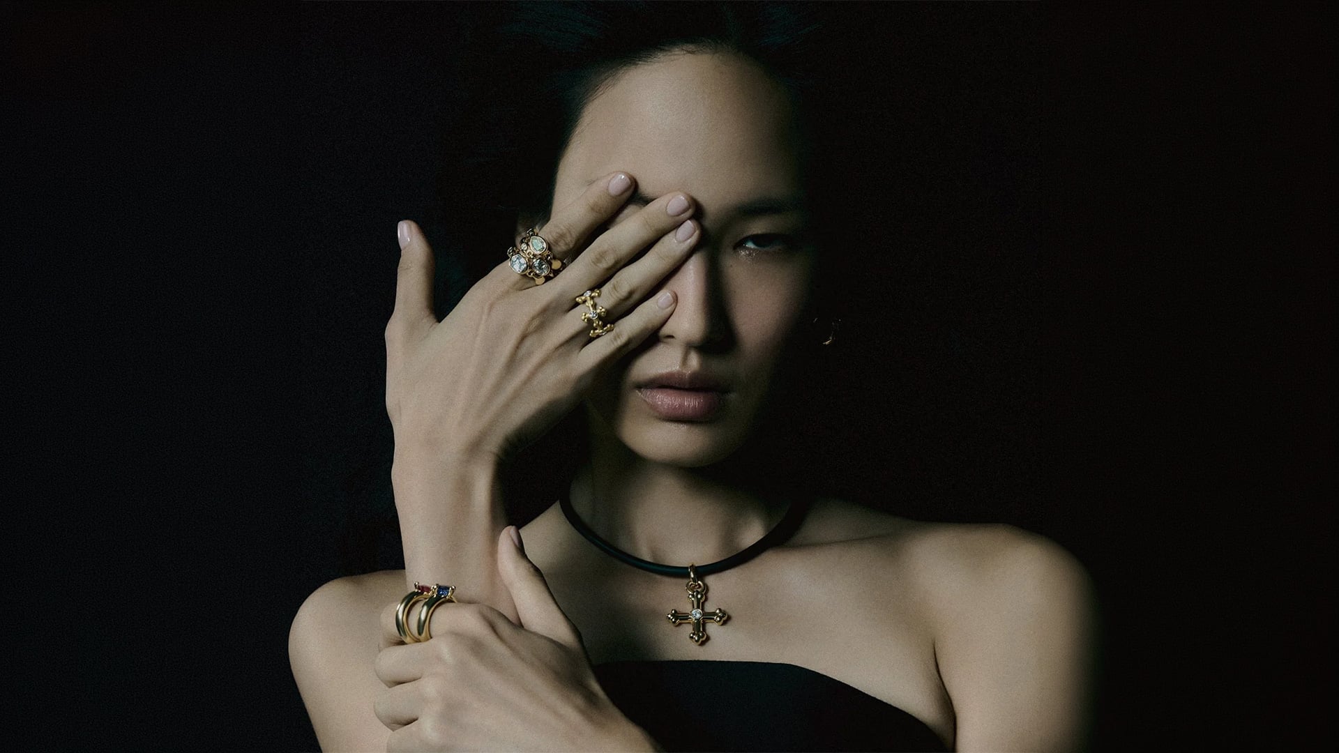 Woman wearing gold rings and cross pendant in low light