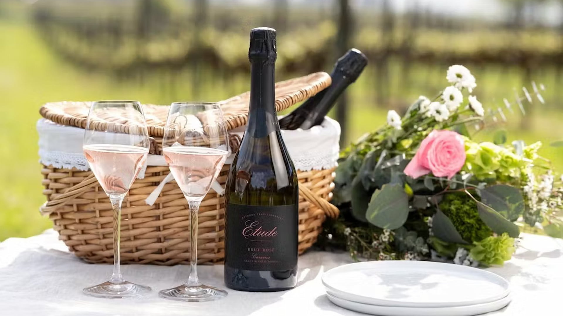 Picnic with wine, flowers, and glasses on table.