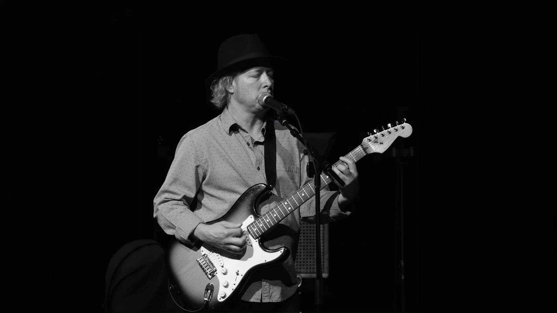 Black-and-white guitarist singing into microphone onstage