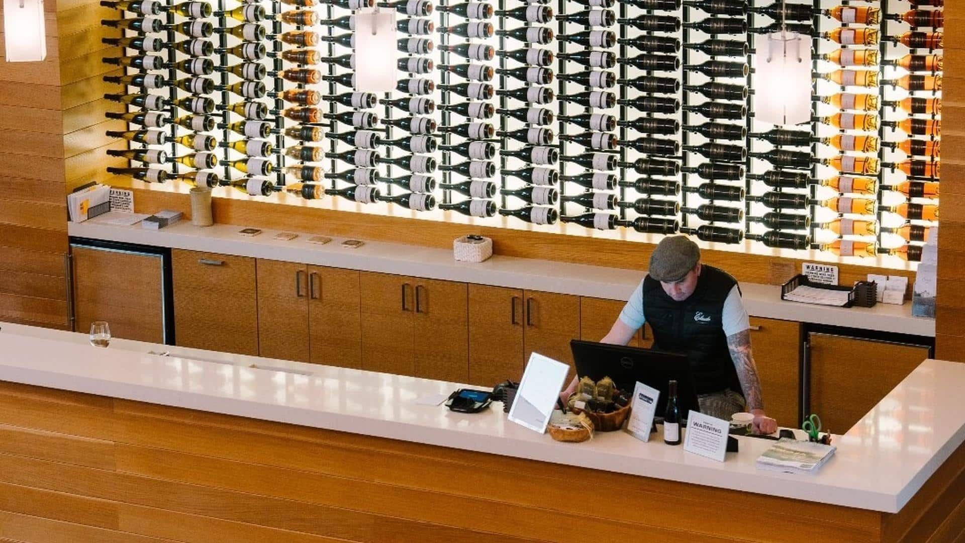Wine tasting room with bottle display and worker.