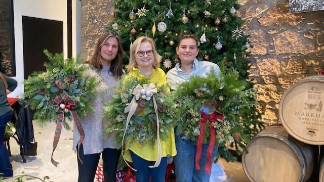 Three people holding wreaths by a Christmas tree.