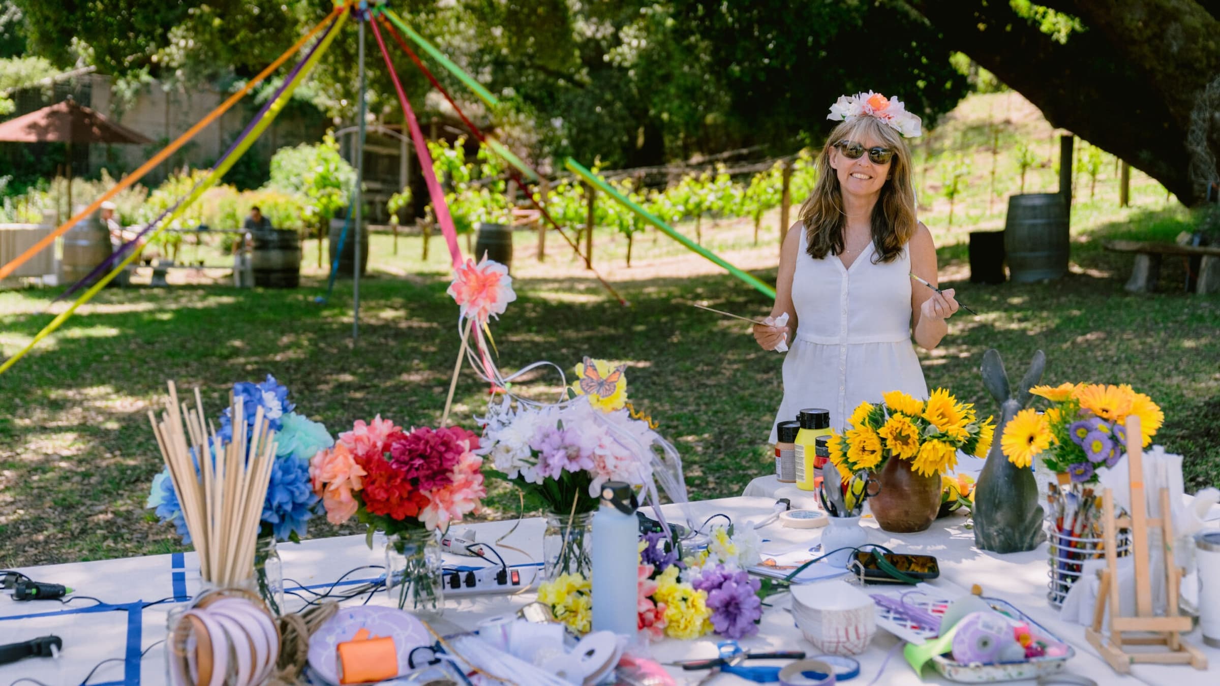Woman at outdoor craft table with flowers and supplies.