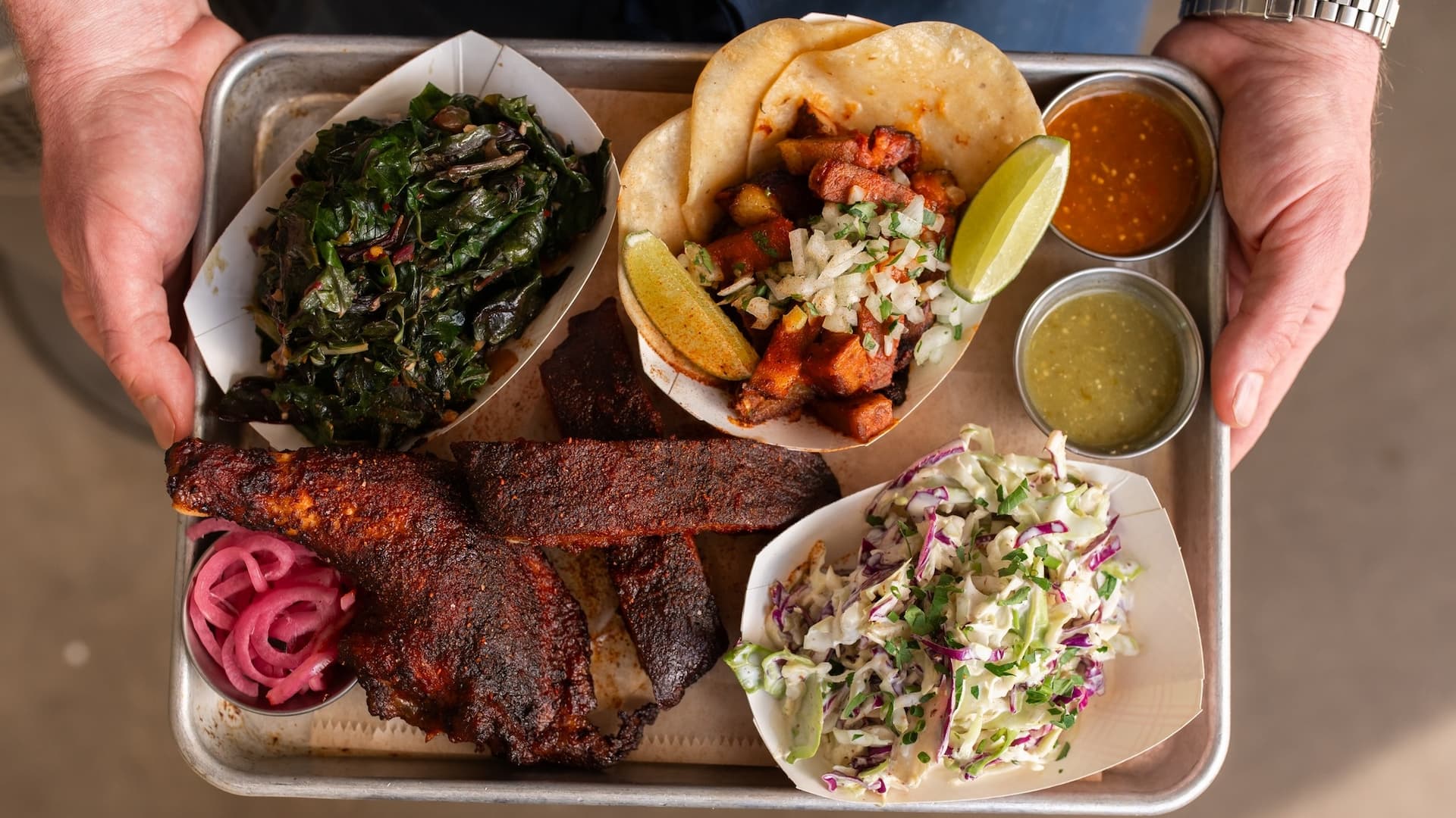 Tray with tacos, ribs, greens, coleslaw, and sauces.