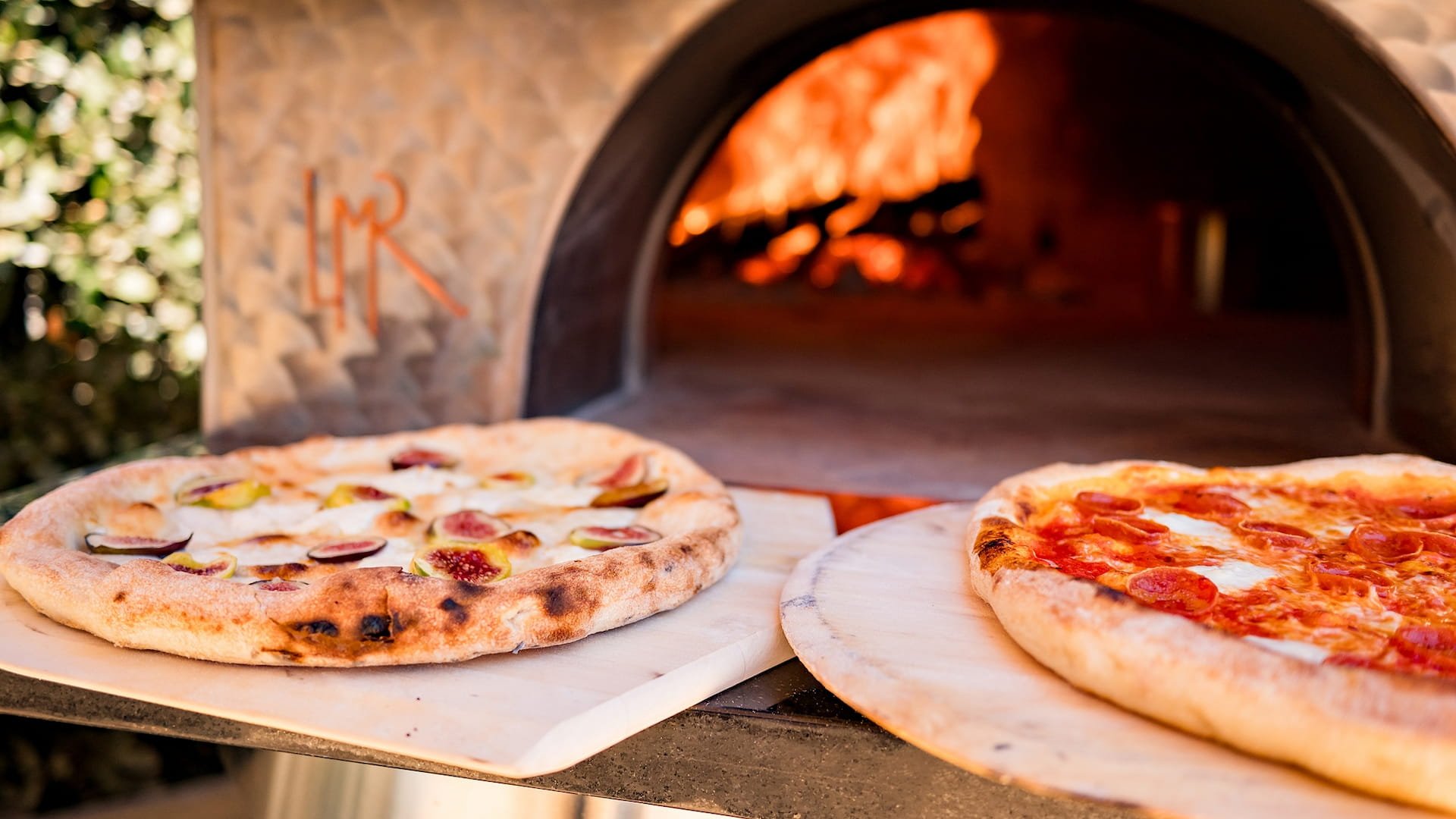 Wood-fired pizzas being cooked in rustic oven.