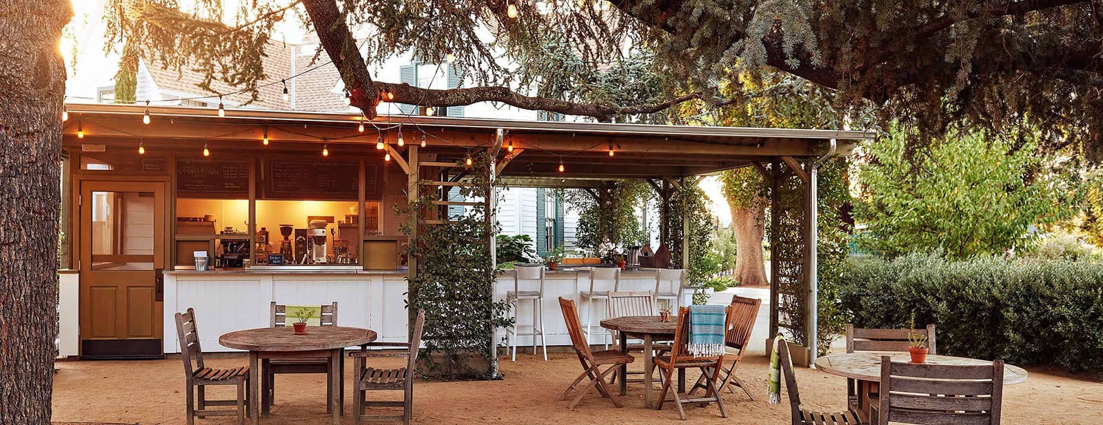 Outdoor cafe seating with string lights and greenery.