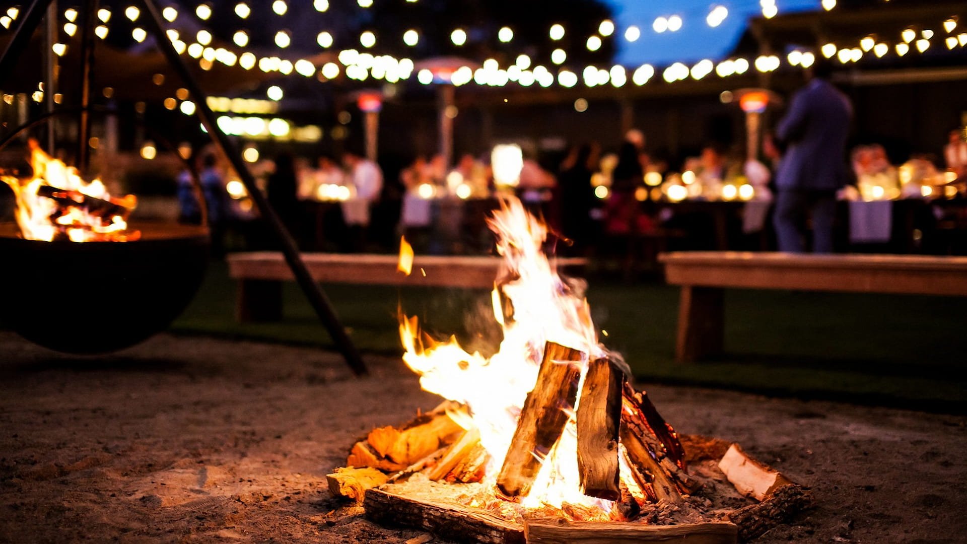 Cozy outdoor night event with fire pit and lights.
