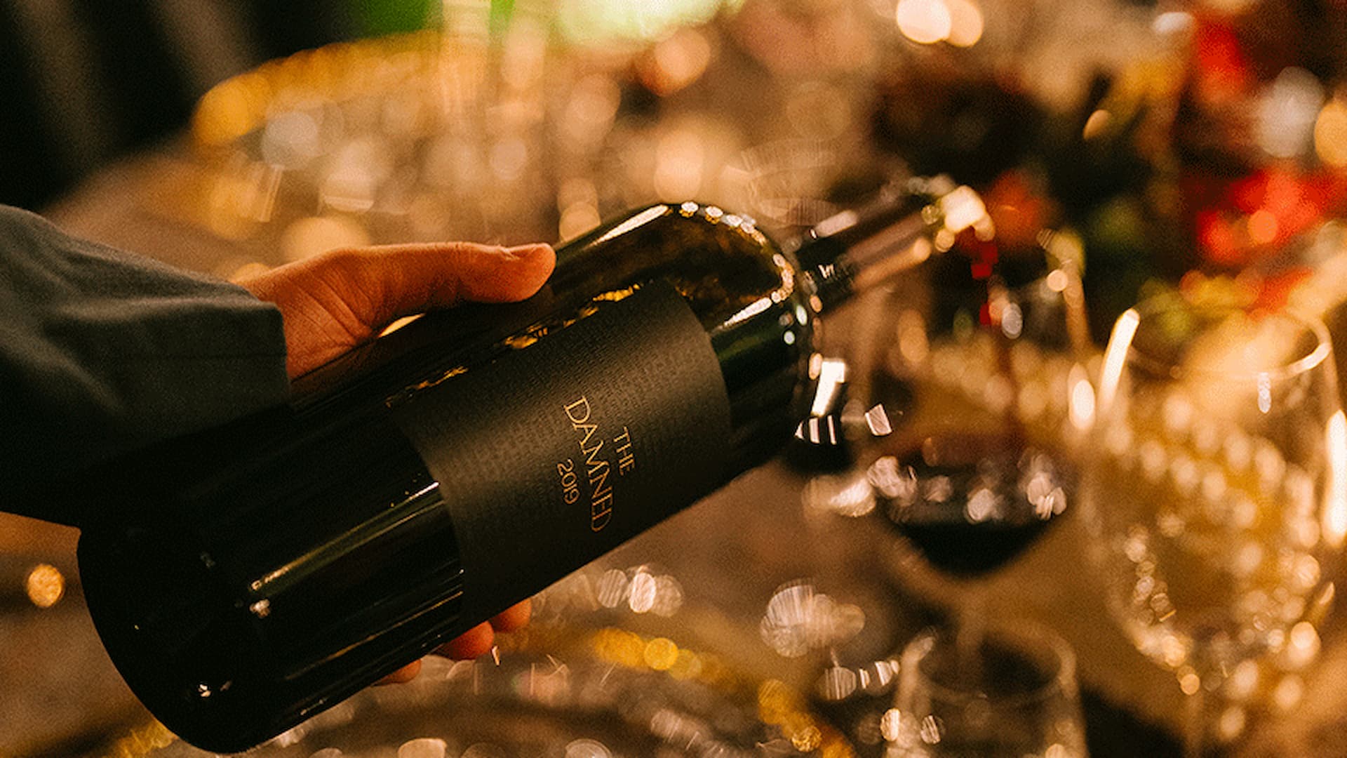 Hand holding a wine bottle at dinner table.
