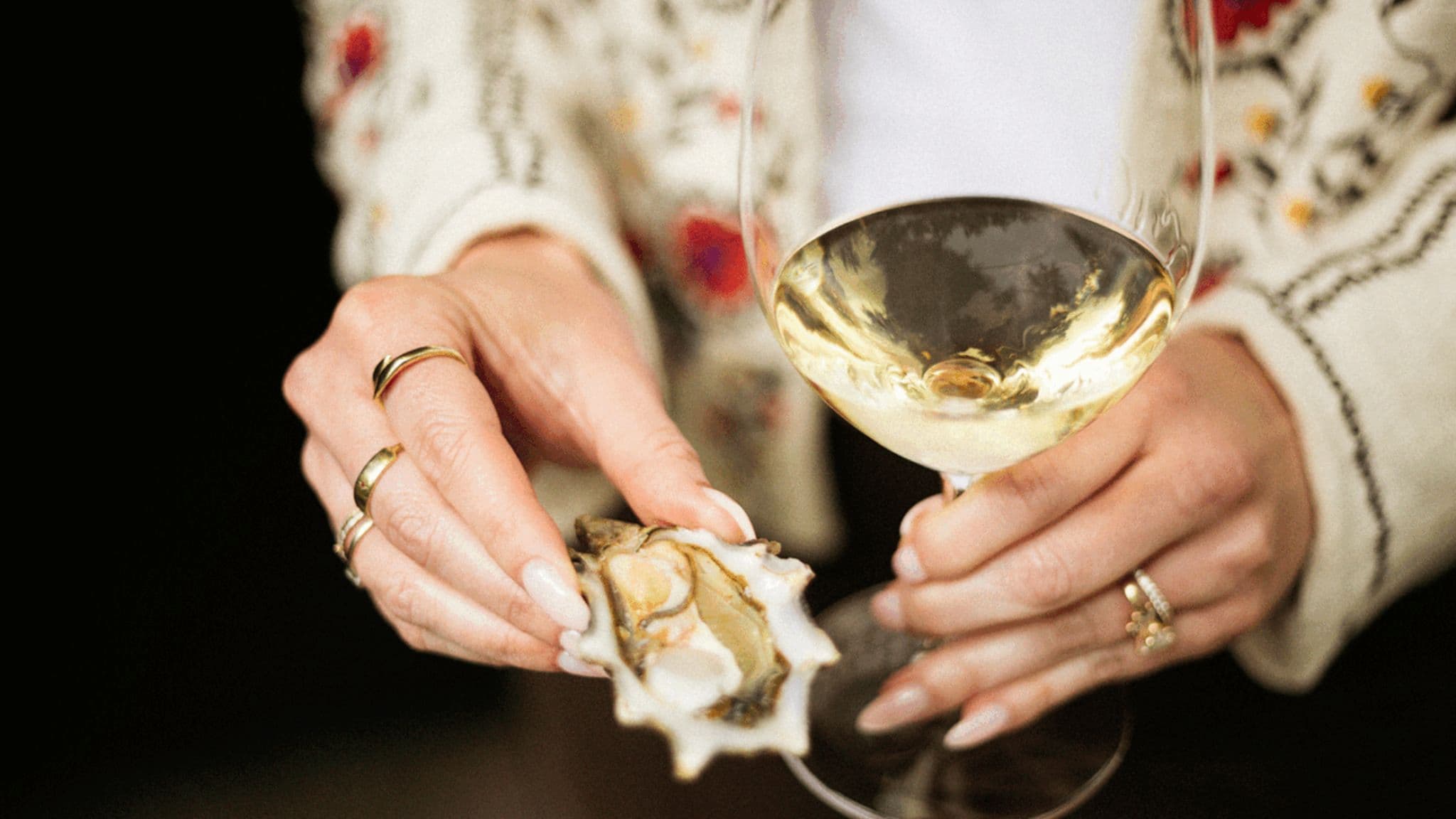 Hands holding oyster and glass of white wine