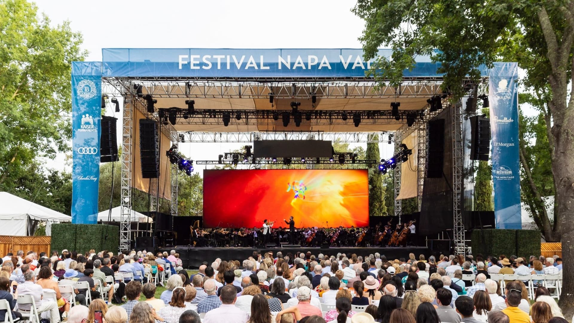 Outdoor music festival with orchestra performing on stage.