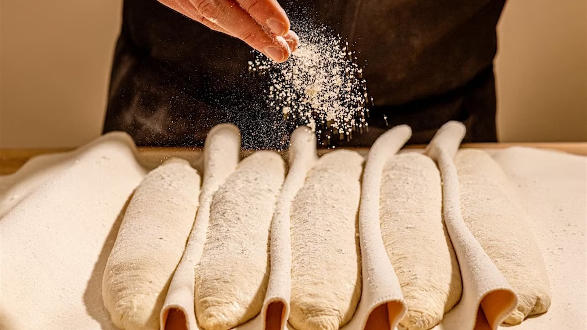 Baker sprinkling flour on proofed dough loaves.