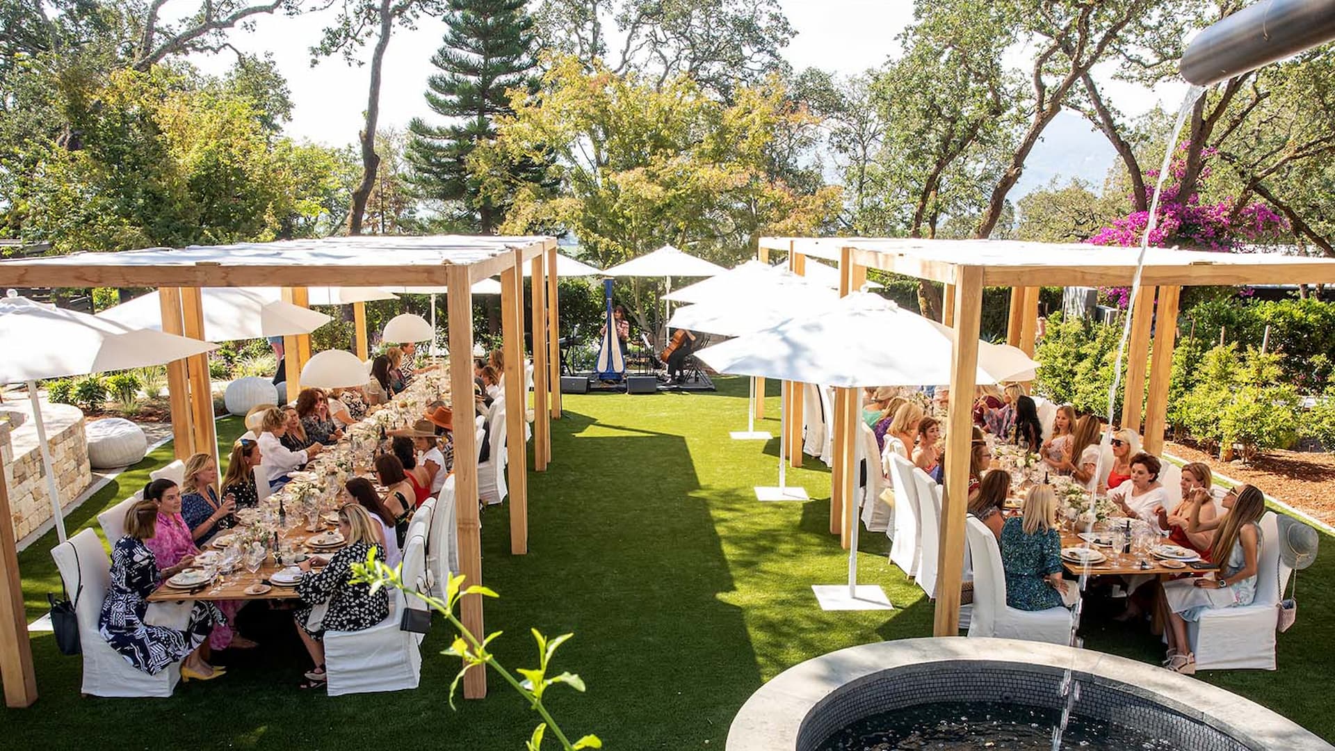 Outdoor garden party with people dining under umbrellas.