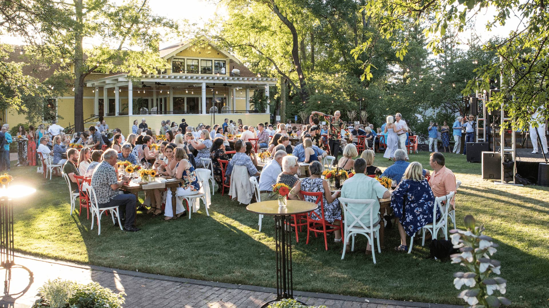 Outdoor gathering at garden event with tables and dancing.
