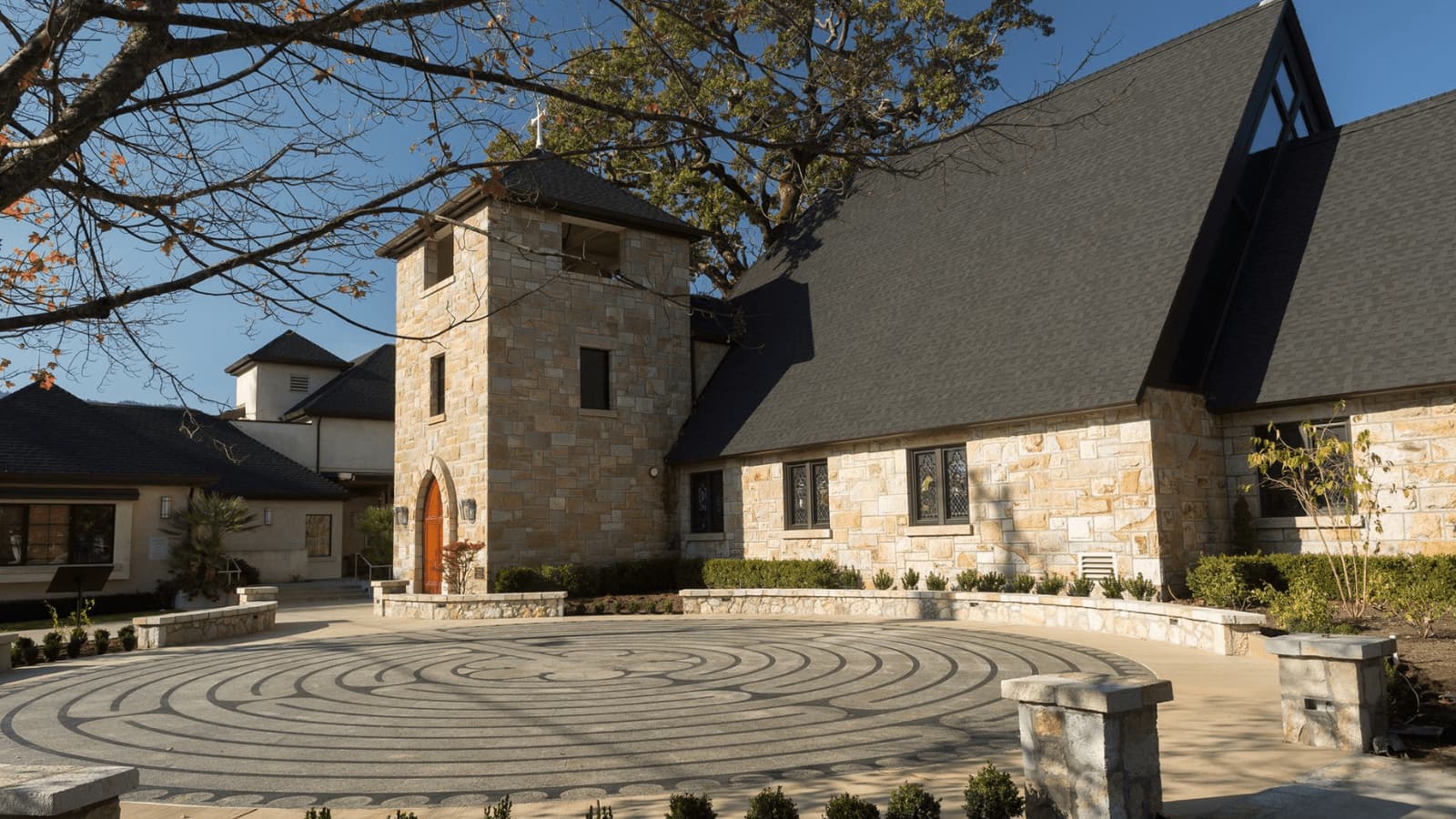Stone church with circular courtyard under tree branches.