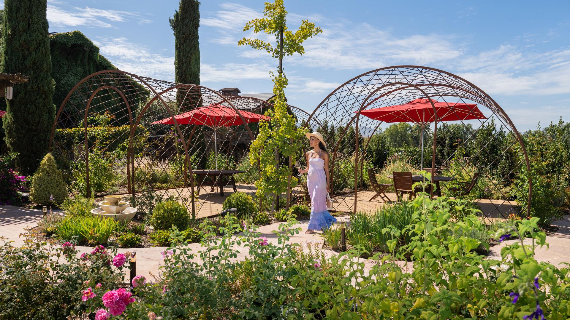 Woman walking in a colorful garden with gazebo.