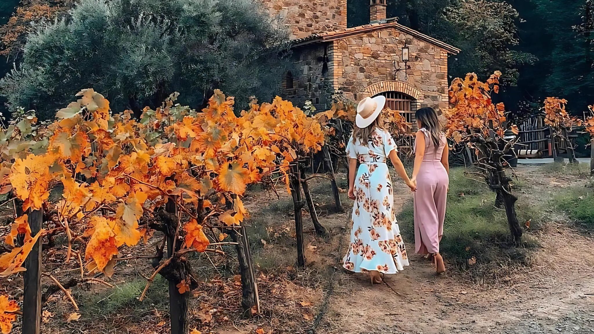 Two women walk through autumn vineyard.