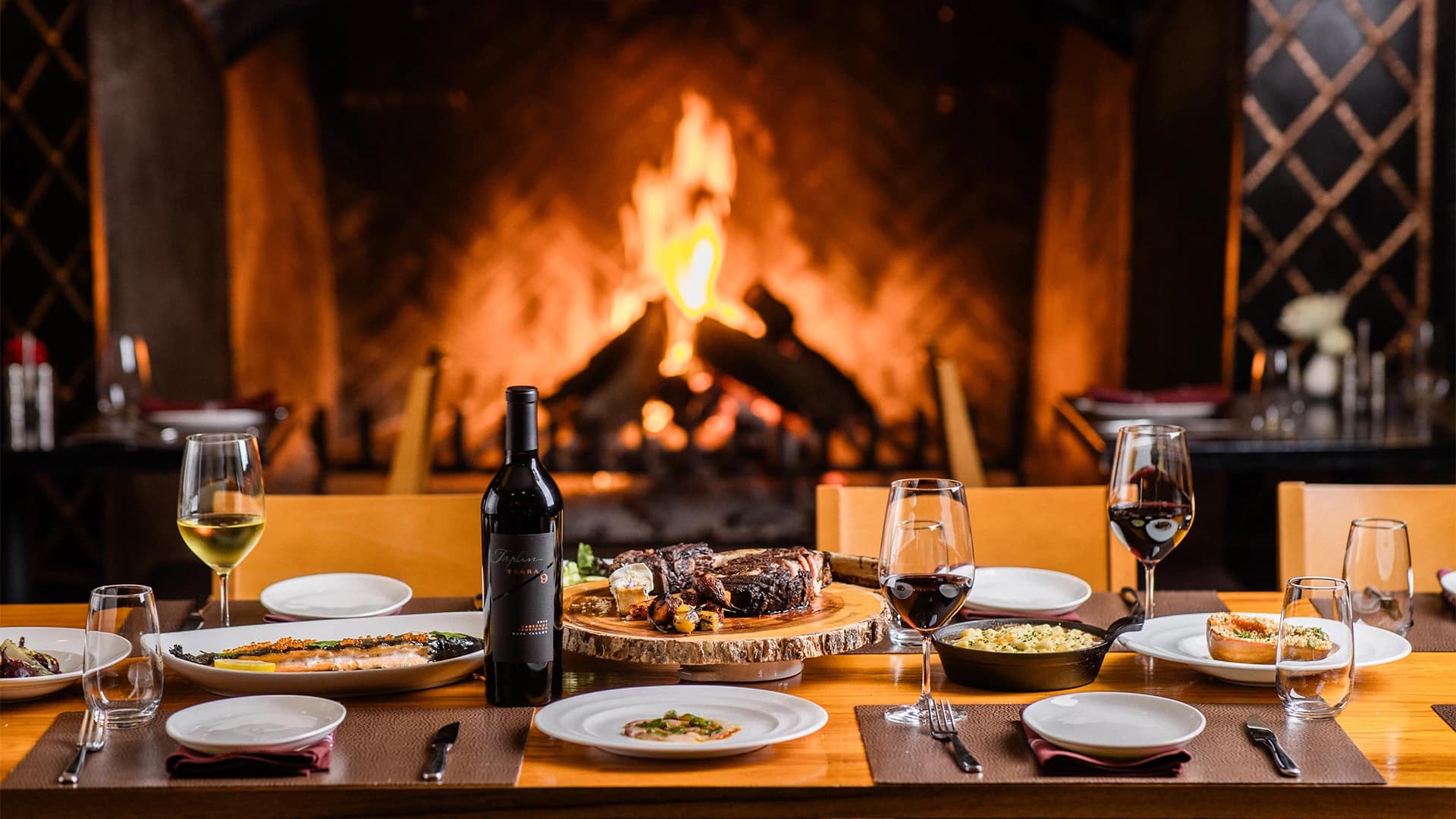 Elegant dining setup with wine by a fireplace.