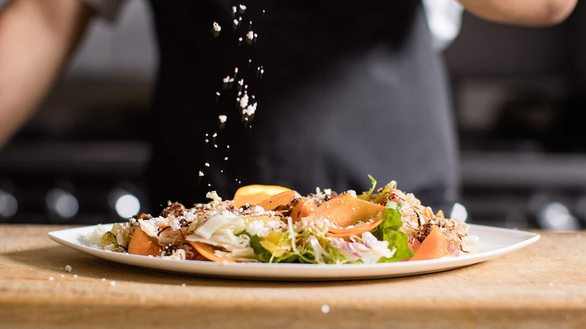 Chef garnishing fresh salad with cheese sprinkles