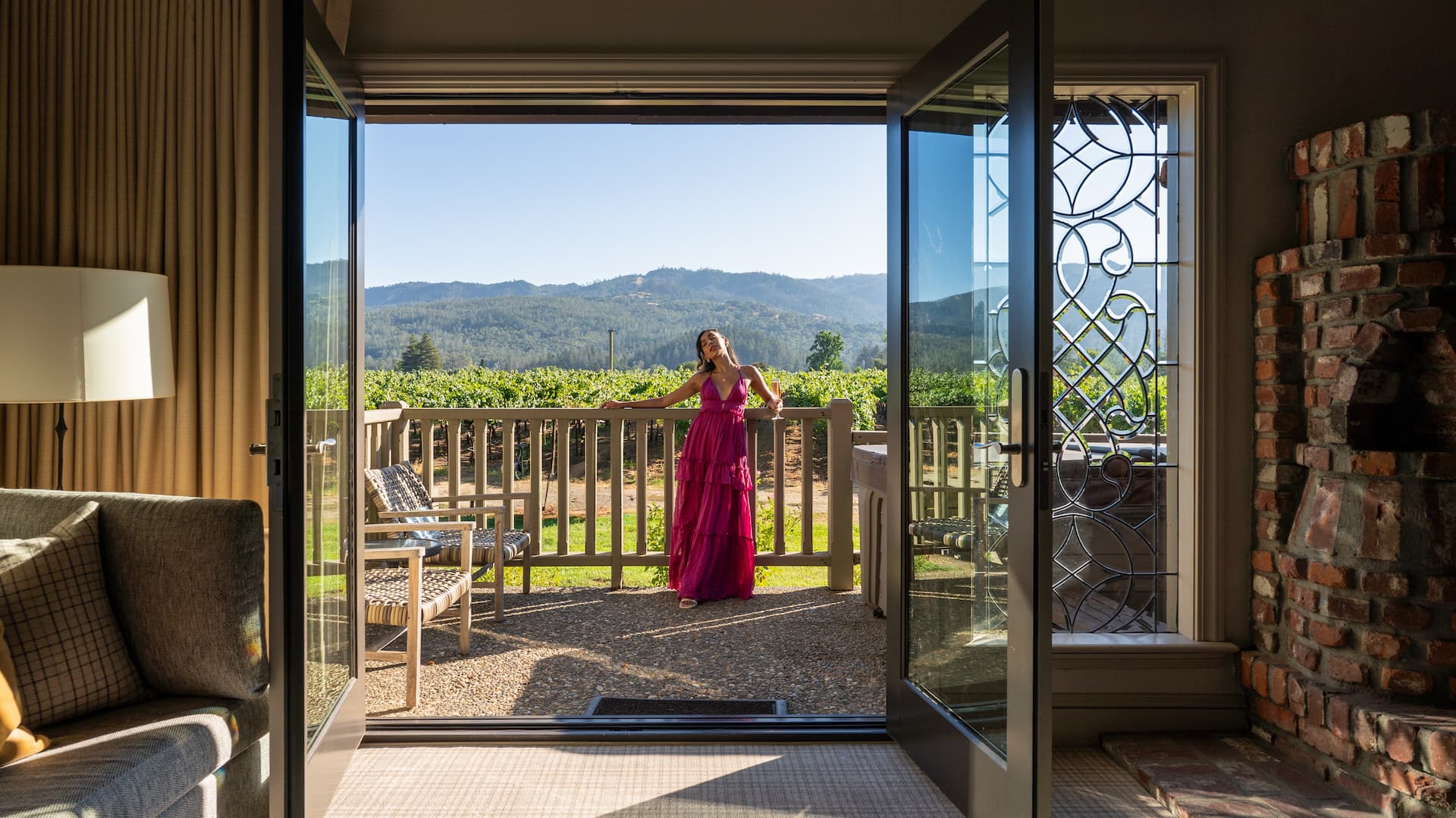 Woman in pink dress on patio with vineyard view.