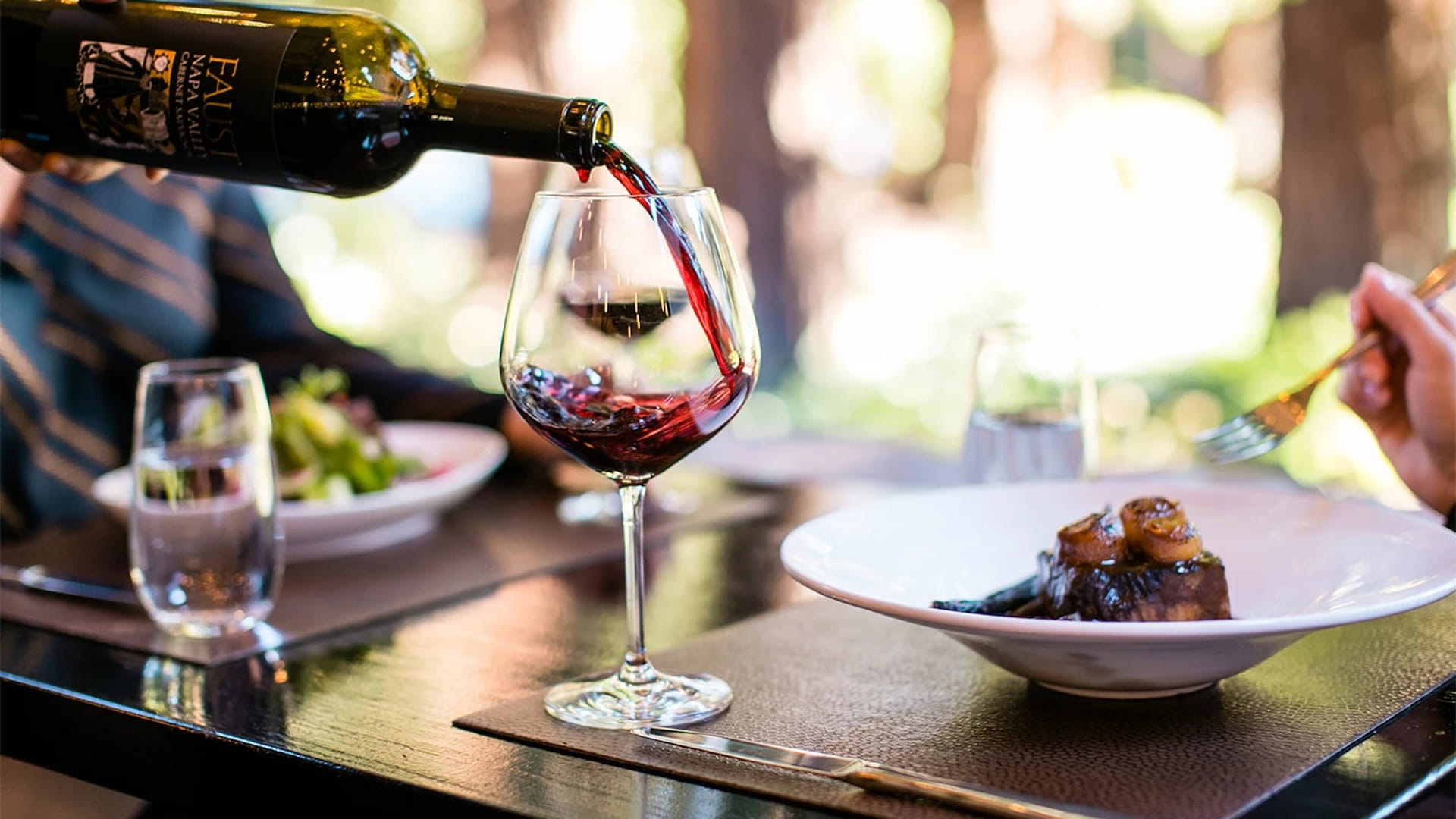 Red wine pouring into glass, elegant dining setting.