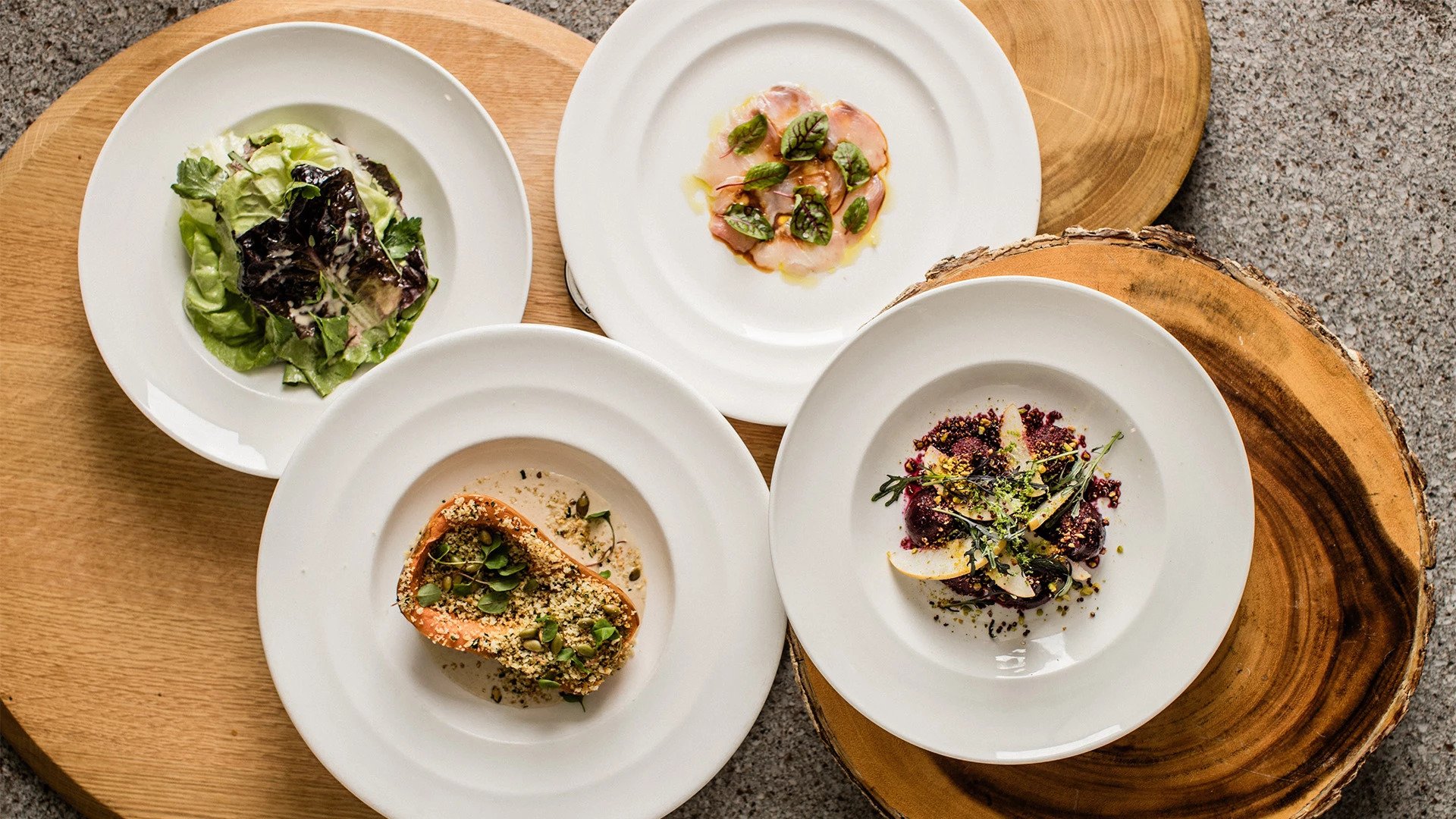 Four gourmet dishes on round wooden platters.