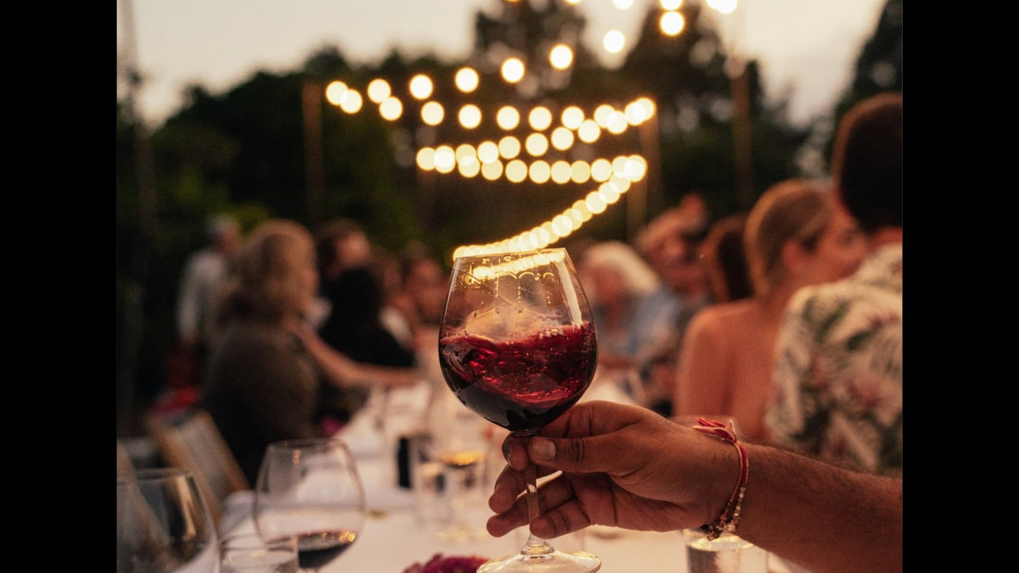 Hand holding red wine at outdoor evening party