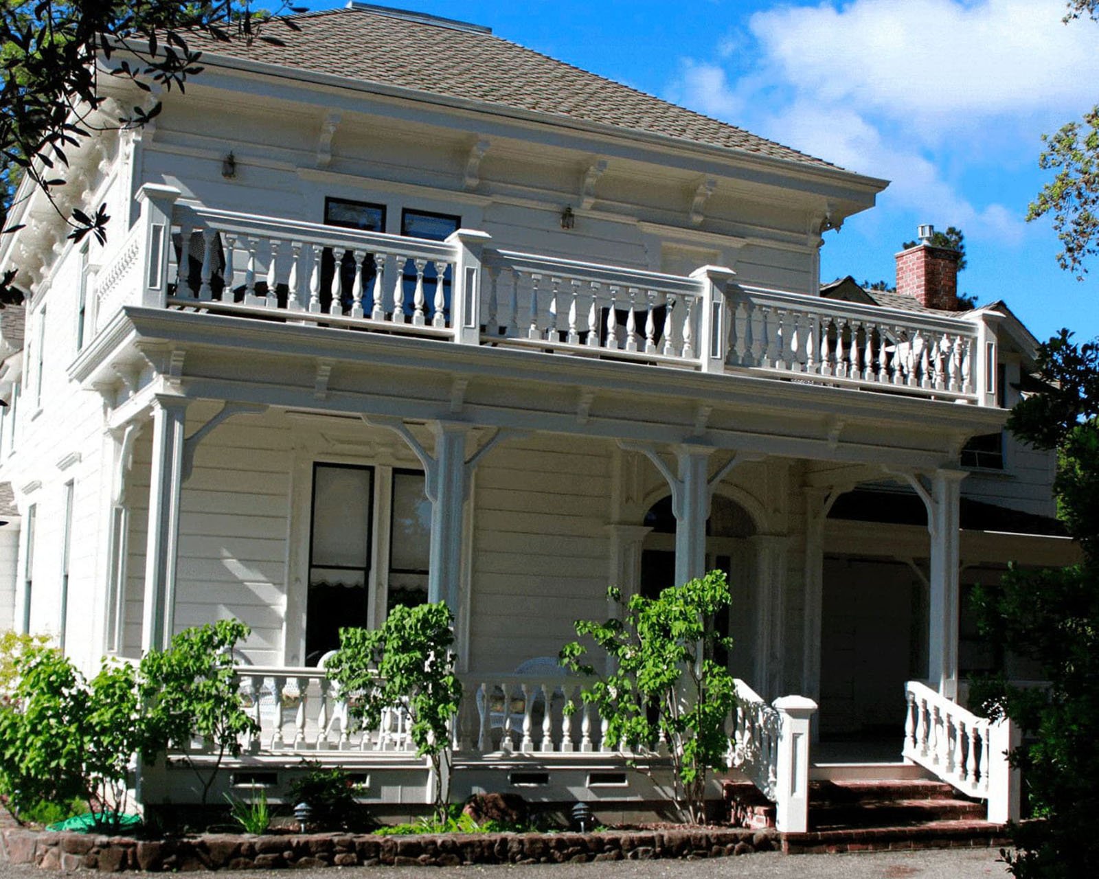 Victorian-style house with balcony and greenery