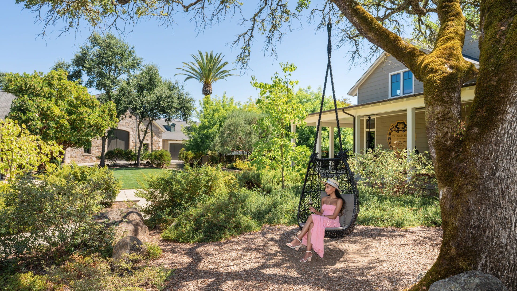 Woman relaxing on garden swing, under trees.