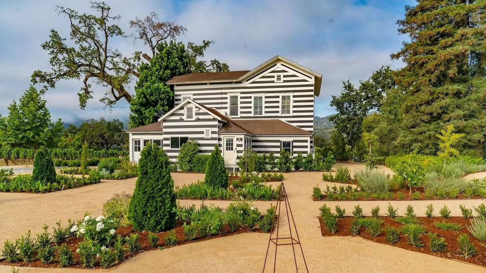 Black and white striped farmhouse with landscaped garden