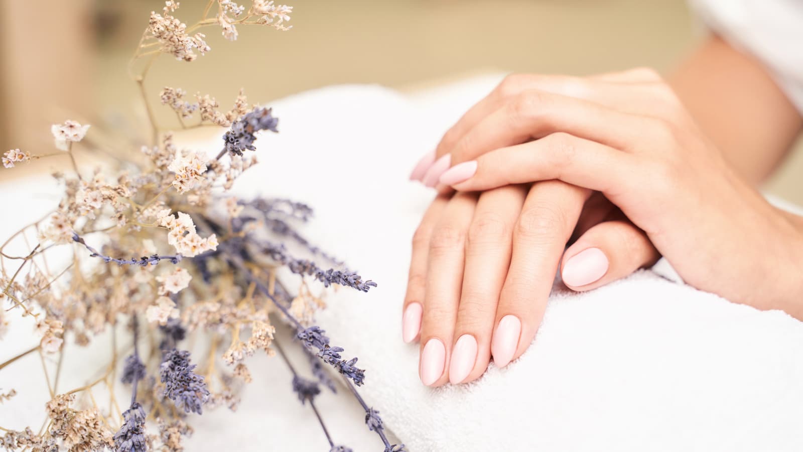 Manicured hands with lavender flowers on towel.