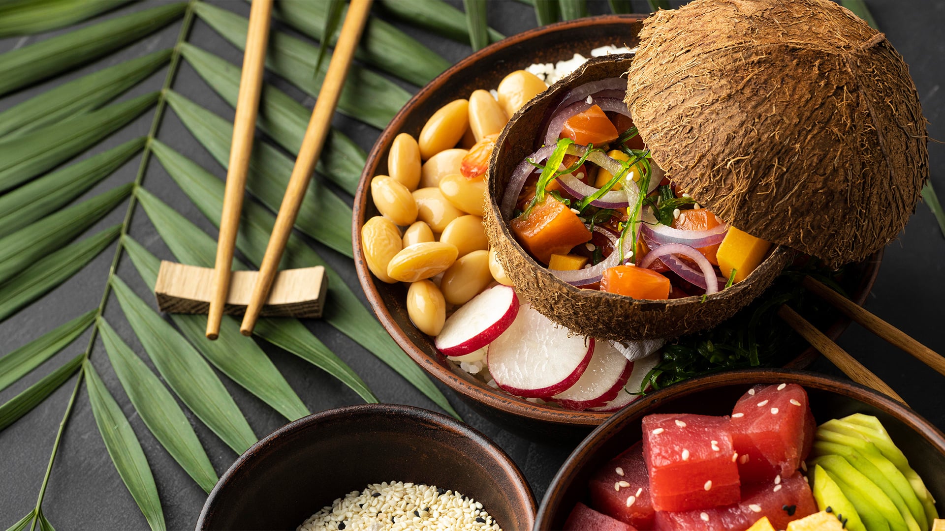 Coconut bowl of poke ingredients with chopsticks and tropical leaves