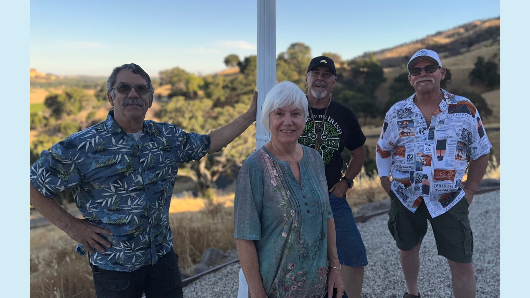 Four adults posing outdoors with scenic hills backdrop