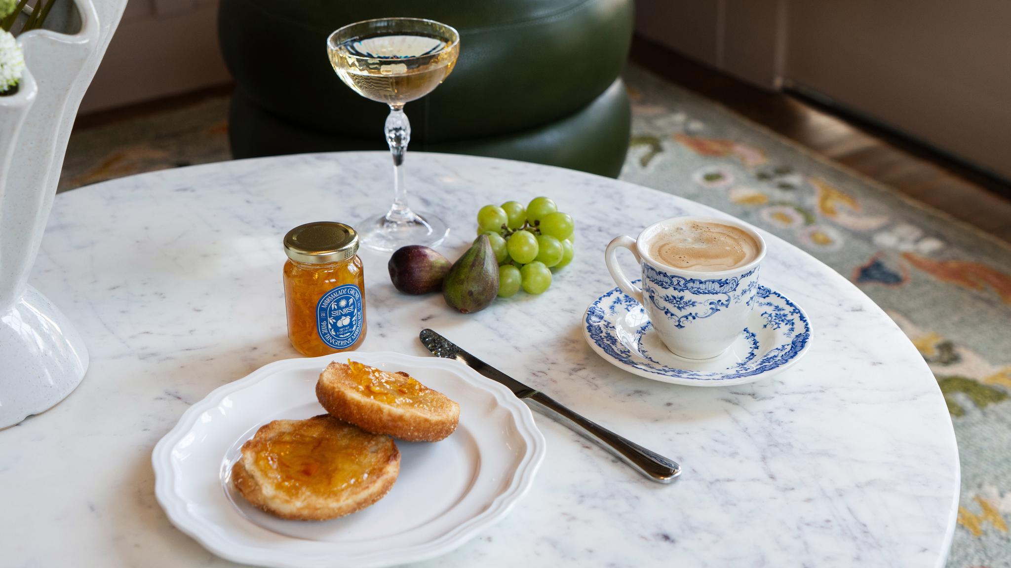 Breakfast with toast, jam, coffee, and fruit on table.