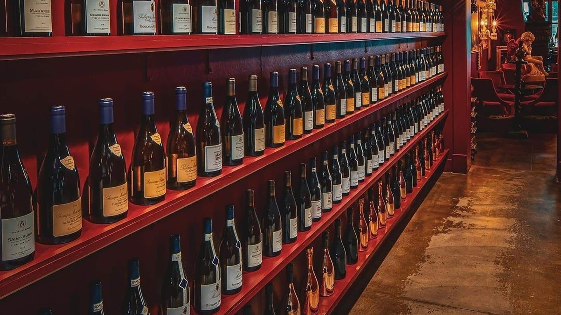 Wine bottles on red shelves in dimly lit room.