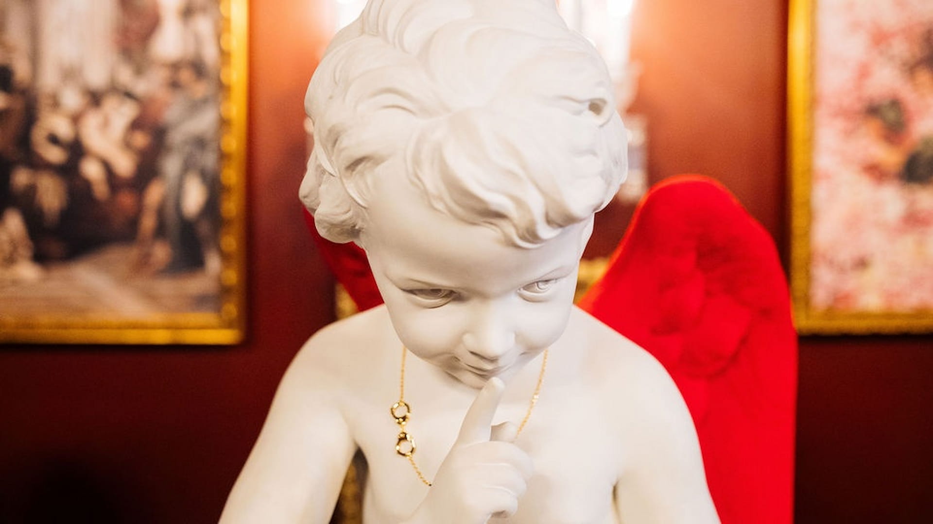 White statue of cherub with red background.