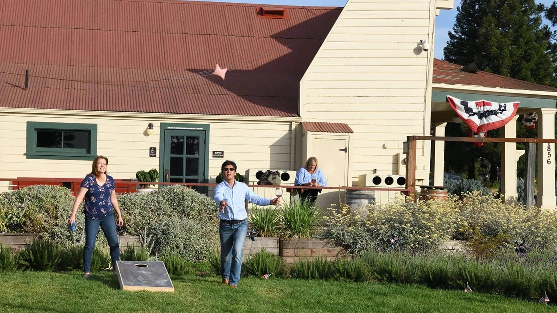 People playing cornhole in backyard with drinks.