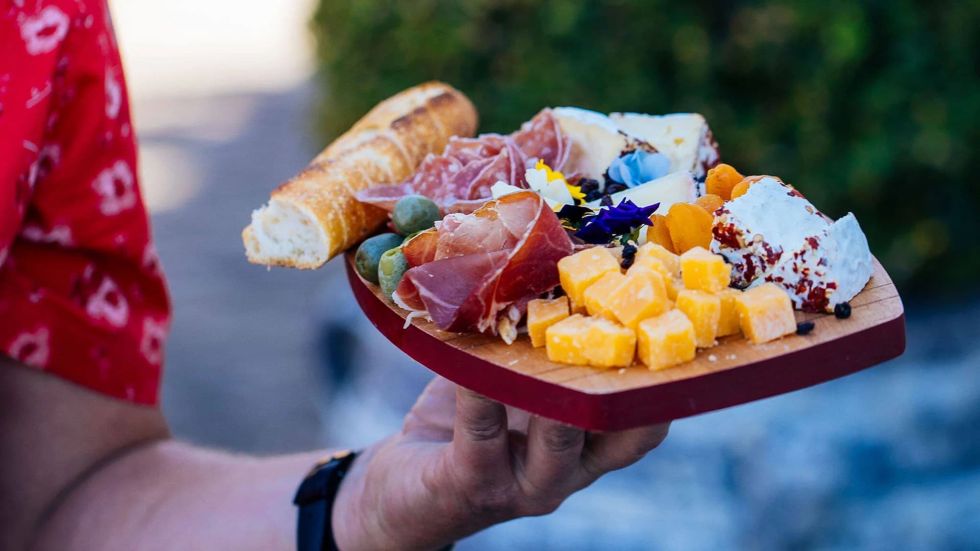 Charcuterie board with meats, cheeses, bread, and flowers.