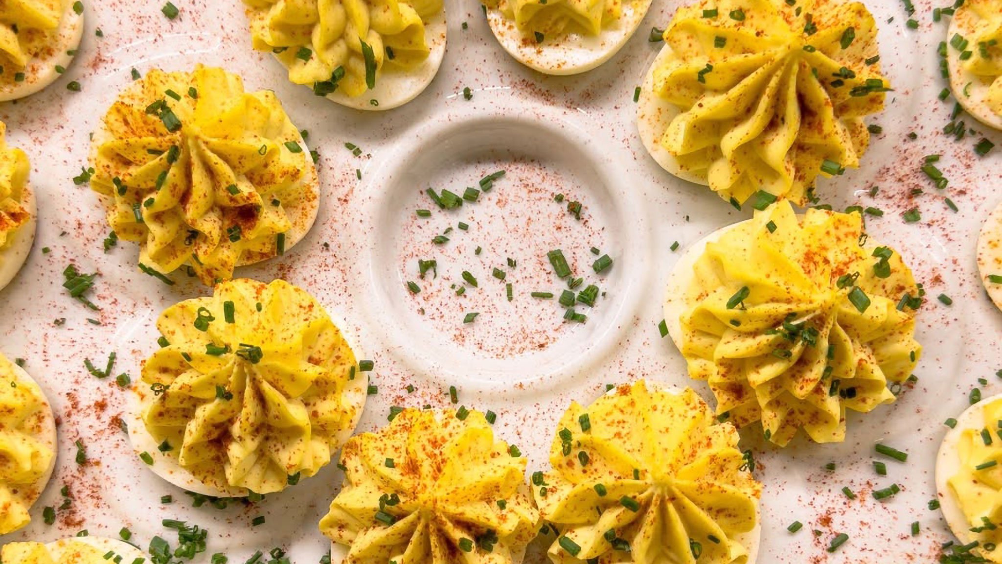Deviled eggs with paprika and chives on platter.
