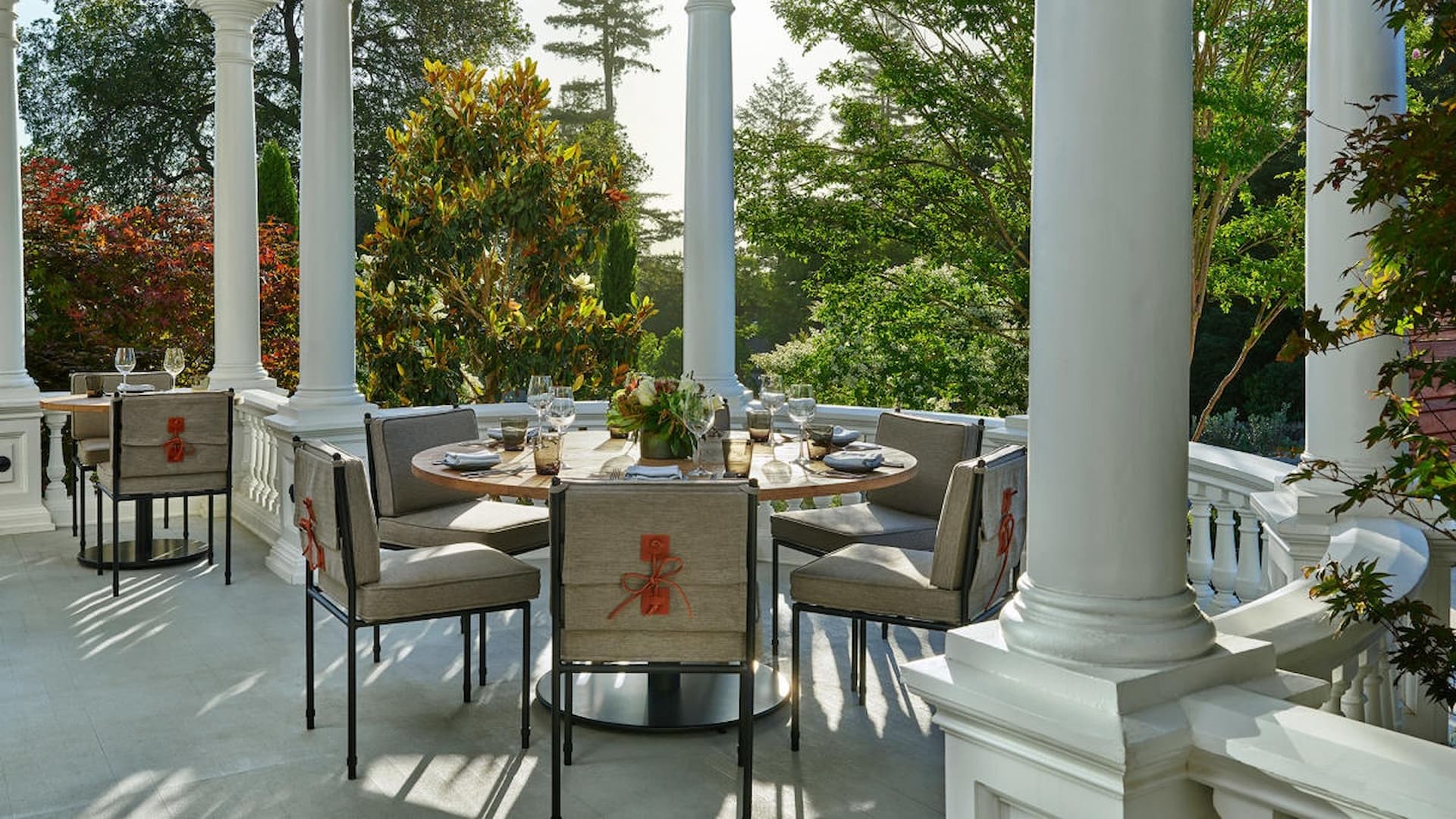 Outdoor dining on elegant porch surrounded by trees.