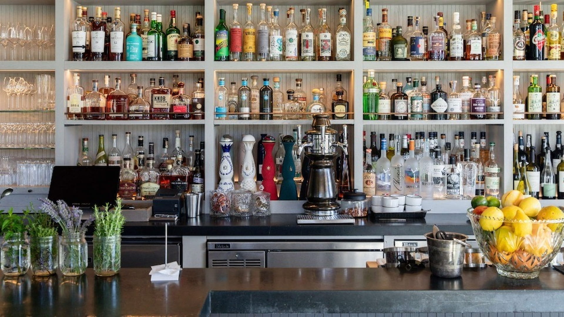 Well-stocked bar with bottles and fresh herbs.