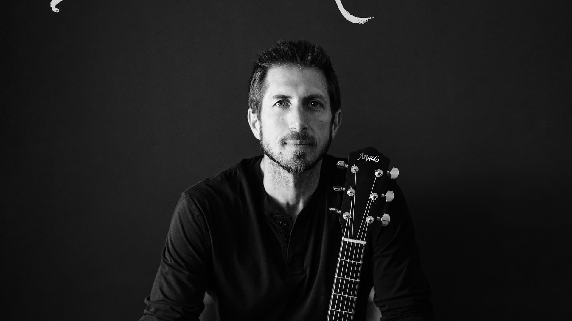 Man with guitar sitting, black and white photo.