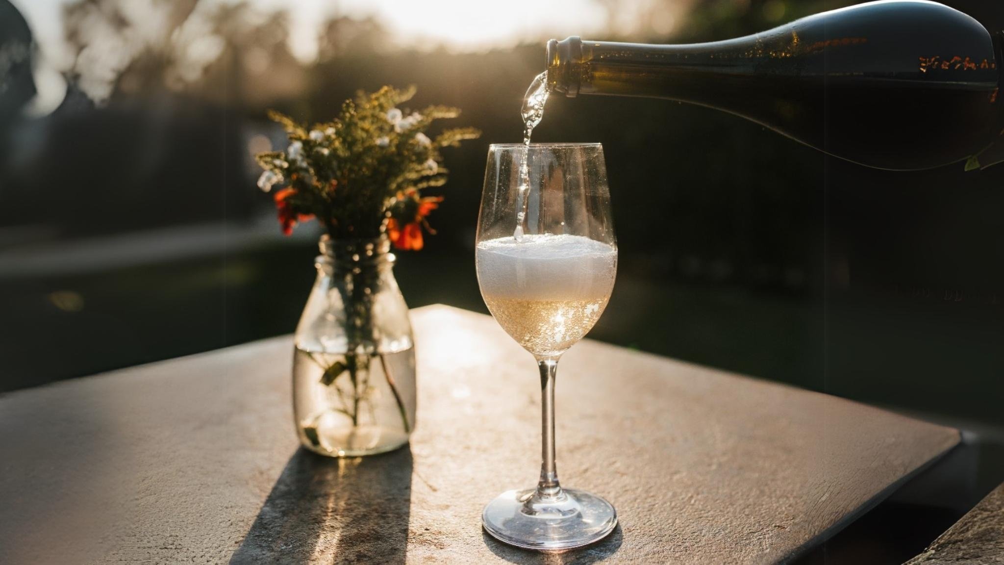 Pouring sparkling wine into glass next to flowers.