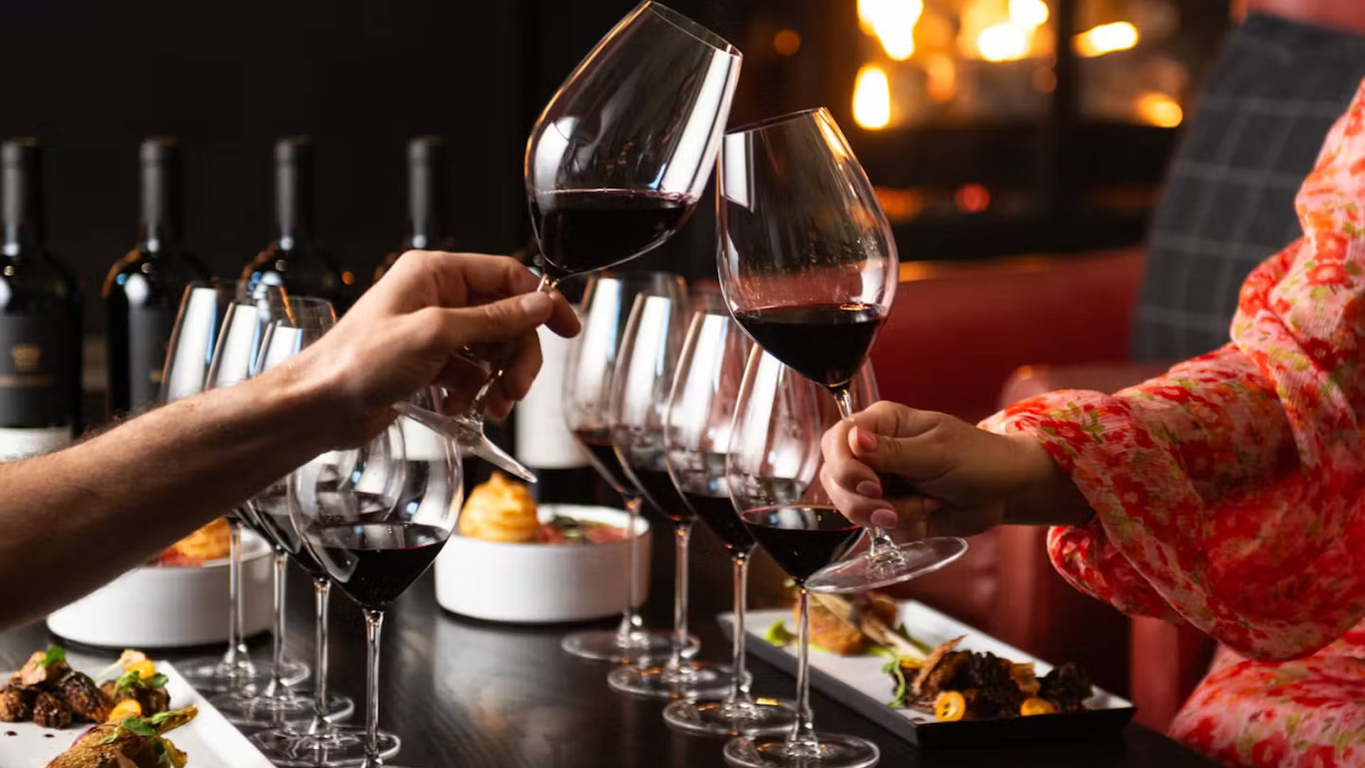 People toasting with red wine at dinner party.