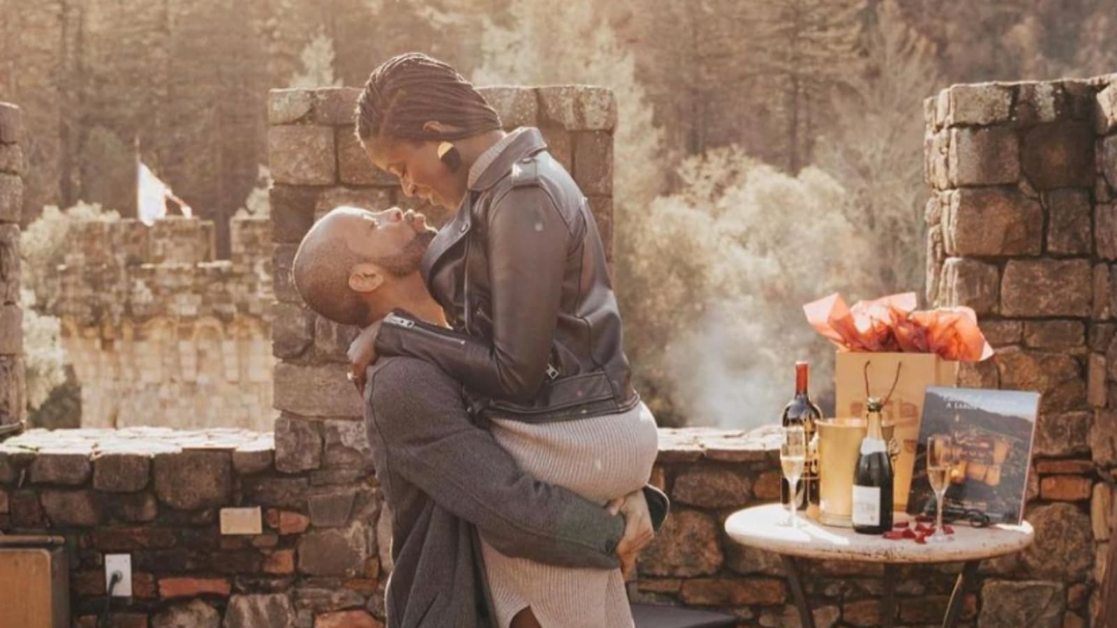 Couple embracing near wine, outdoor setting.